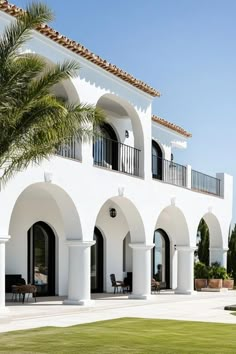 a large white house with palm trees in the front yard and patio area, on a sunny day