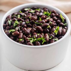 a white bowl filled with black beans and garnished with green leaves on top