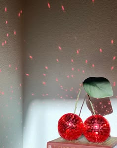 two shiny red disco balls sit on top of a book with a green leaf sticking out of it