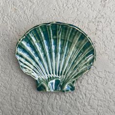 a green shell shaped dish hanging on the side of a white wall with grey paint