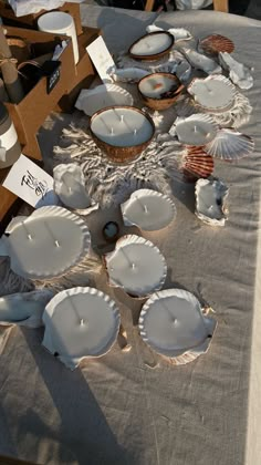 several white dishes and candles on a table with other items in the background at an outdoor market