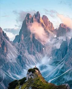 the mountains are covered in clouds and green grass, with a person standing on top