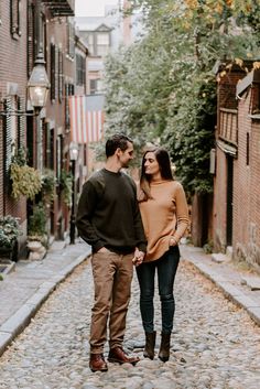 an engaged couple standing on cobblestone street holding hands and looking at each other