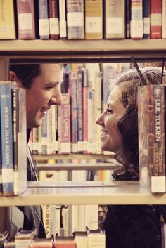 a man and woman looking at each other through the window of a bookshelf