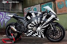 a black and white motorcycle parked in front of a wall with graffiti on it's side