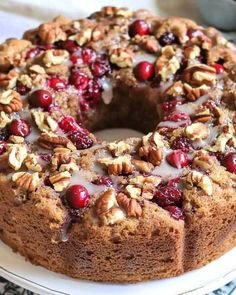 a bundt cake with nuts and cranberries is on a white platter