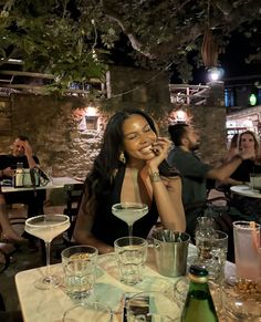 a woman sitting at a table talking on a cell phone with wine glasses in front of her