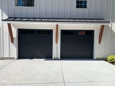 two garage doors are open in front of a white building with black trim on the roof