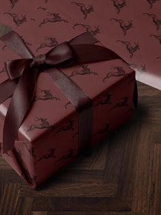 a red gift box with a brown ribbon on top of wooden floor next to wallpaper