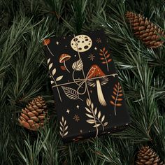 a present wrapped in black paper sitting on top of a tree next to pine cones