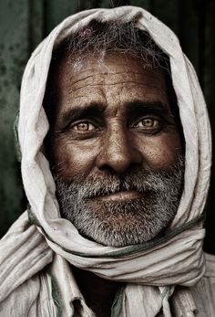 an old man wearing a white scarf and looking at the camera