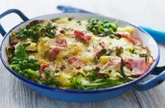 a casserole dish with ham, broccoli and peas in it on a wooden table