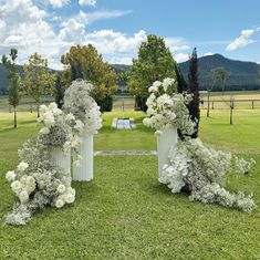 three white vases filled with flowers sitting on top of a lush green field