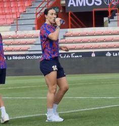 two women in blue and red uniforms standing on a soccer field, one holding a microphone to her mouth