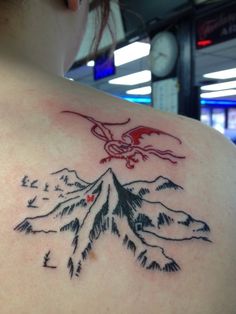 a woman with a tattoo on her shoulder and mountains in the background, is looking at something