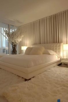 a large white bed sitting in a bedroom next to a tall vase with flowers on it