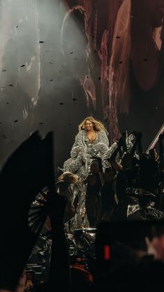 the singer is performing on stage with her hands up in front of her and people behind her