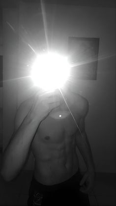 a shirtless man taking a selfie in front of a mirror with the light shining on him