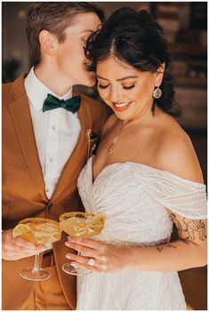 a bride and groom holding champagne glasses in front of each other with their faces close together