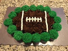 a football shaped cake with green and brown frosting on a silver platter sitting on a granite countertop