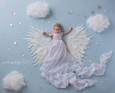 a baby girl dressed in white with angel wings and stars around her body on a blue background