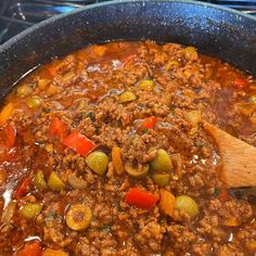 a pot filled with meat and vegetables on top of a stove next to a wooden spoon