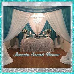 a table set up for an event with white linens and teal blue drapes