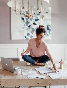 a woman sitting at a table with a laptop and papers in front of her on the floor