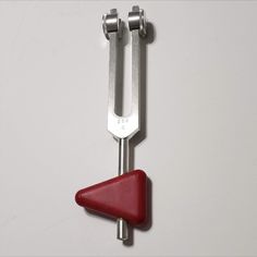 a red triangle shaped object hanging from a hook on a white wall next to a pair of wrenches