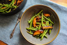 a bowl filled with green beans and mushrooms next to a skillet on a table