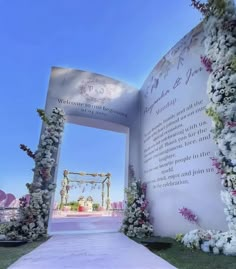 an outdoor wedding ceremony with flowers on the side and a large white sign that says welcome to you