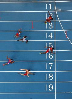 four athletes are competing in a race on a blue track with white lines and numbers