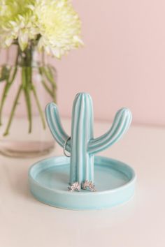 a small cactus ring holder on a table next to a vase with flowers in it