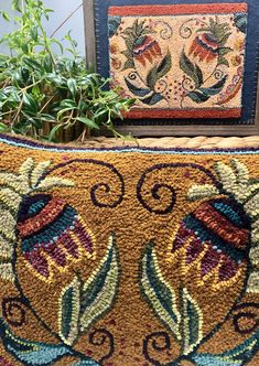 a close up of a pillow on a table near a potted plant and framed artwork