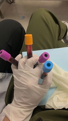 a person in white gloves holding three different colored objects on top of a table next to another persons arm