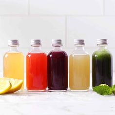 five bottles filled with different colored liquids next to lemon wedges and mint leaves