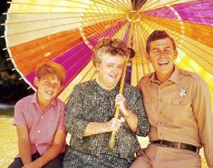 an older man and two younger women sitting under an umbrella