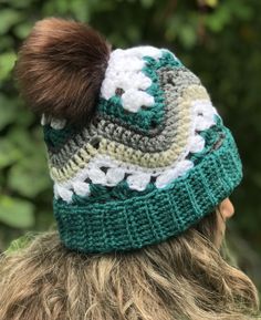 a woman wearing a green and white knitted hat with a brown pom - pom