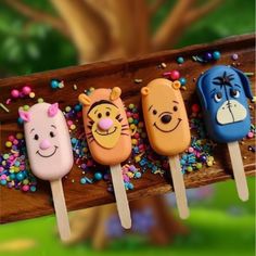 four pops with cartoon faces on them sitting on a wooden stick in front of a tree