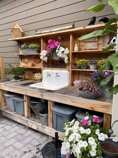 an outdoor garden with potted plants, sink and shelves on the side of a house