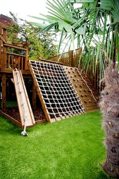 a wooden slide set in the grass next to a palm tree and a large potted plant