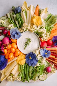 a platter filled with vegetables and dip surrounded by other fruits and veggies