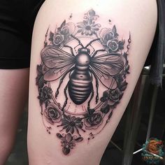 a woman's thigh with a black and white tattoo on it, depicting a bee surrounded by flowers