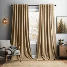 a living room with a chair and window covered in beige drapes next to a painting