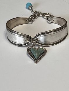 a silver bracelet with a heart charm on the side and a blue bead at the end