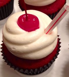 two cupcakes with white frosting and a cherry on top, one has a red striped straw in it