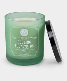 a green candle sitting next to a black lid on a white surface with the words cooling eucalypus printed on it