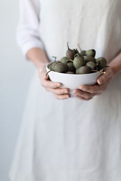 a woman holding a bowl filled with green fruit