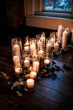 many lit candles on a wooden table in front of a window with leaves scattered around it