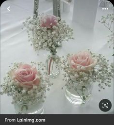 three clear vases with pink roses and baby's breath are on a table